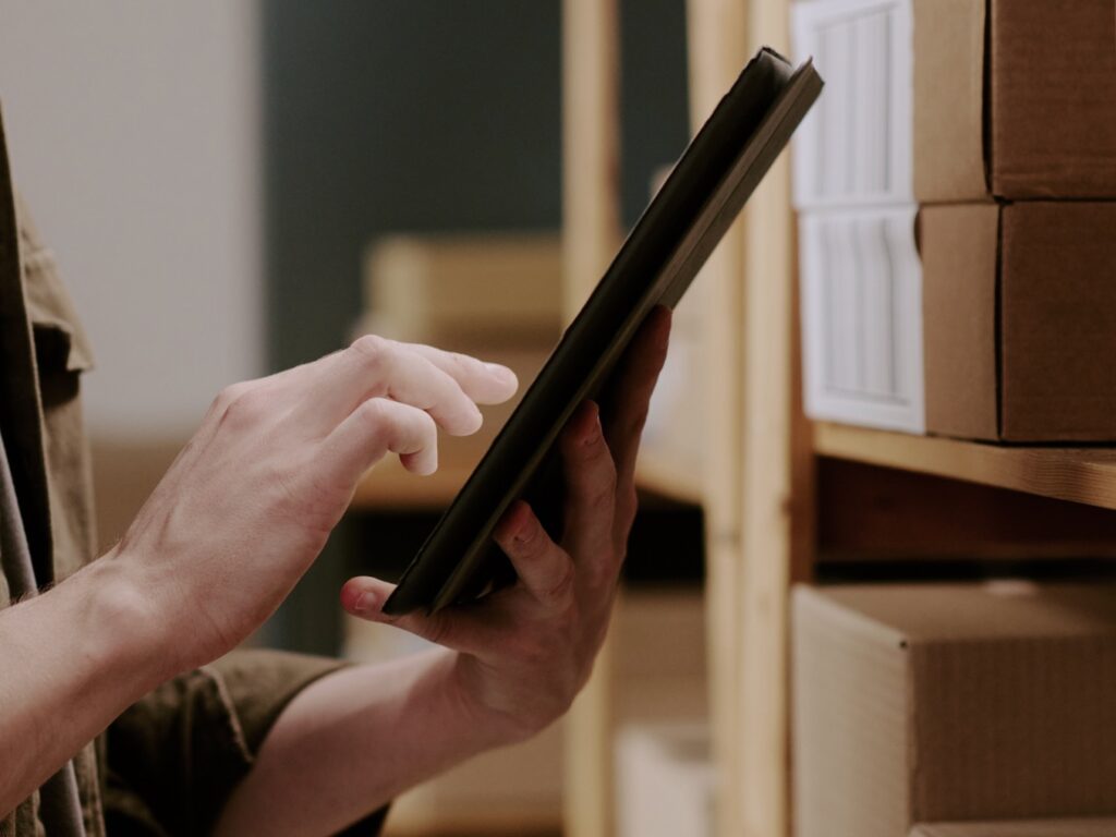 Close-up of a person using tablet with shelves of packaged products in the background.